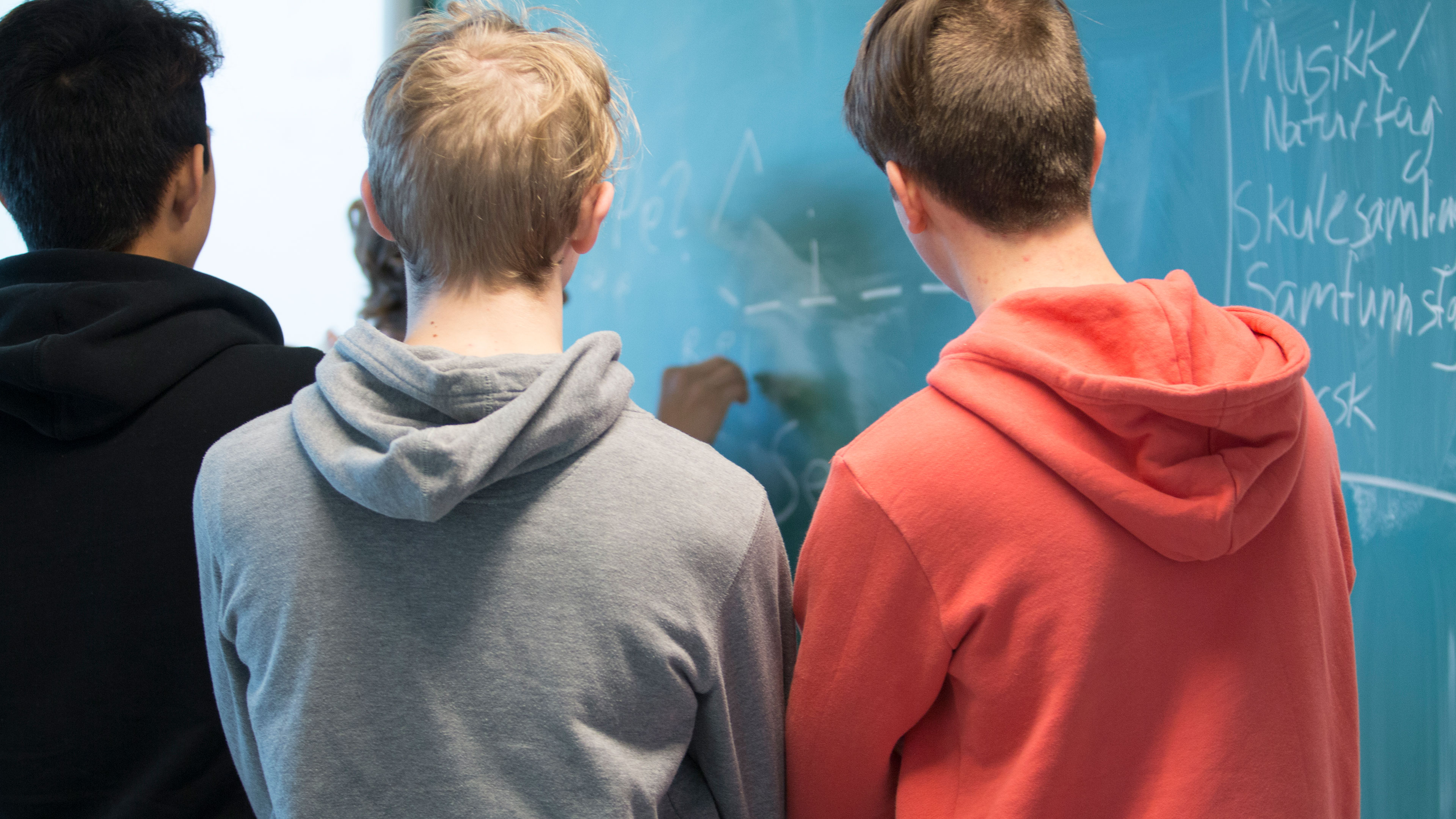 Tre skolelever med ryggen til der skriver på en tavle // Foo: Colourbox