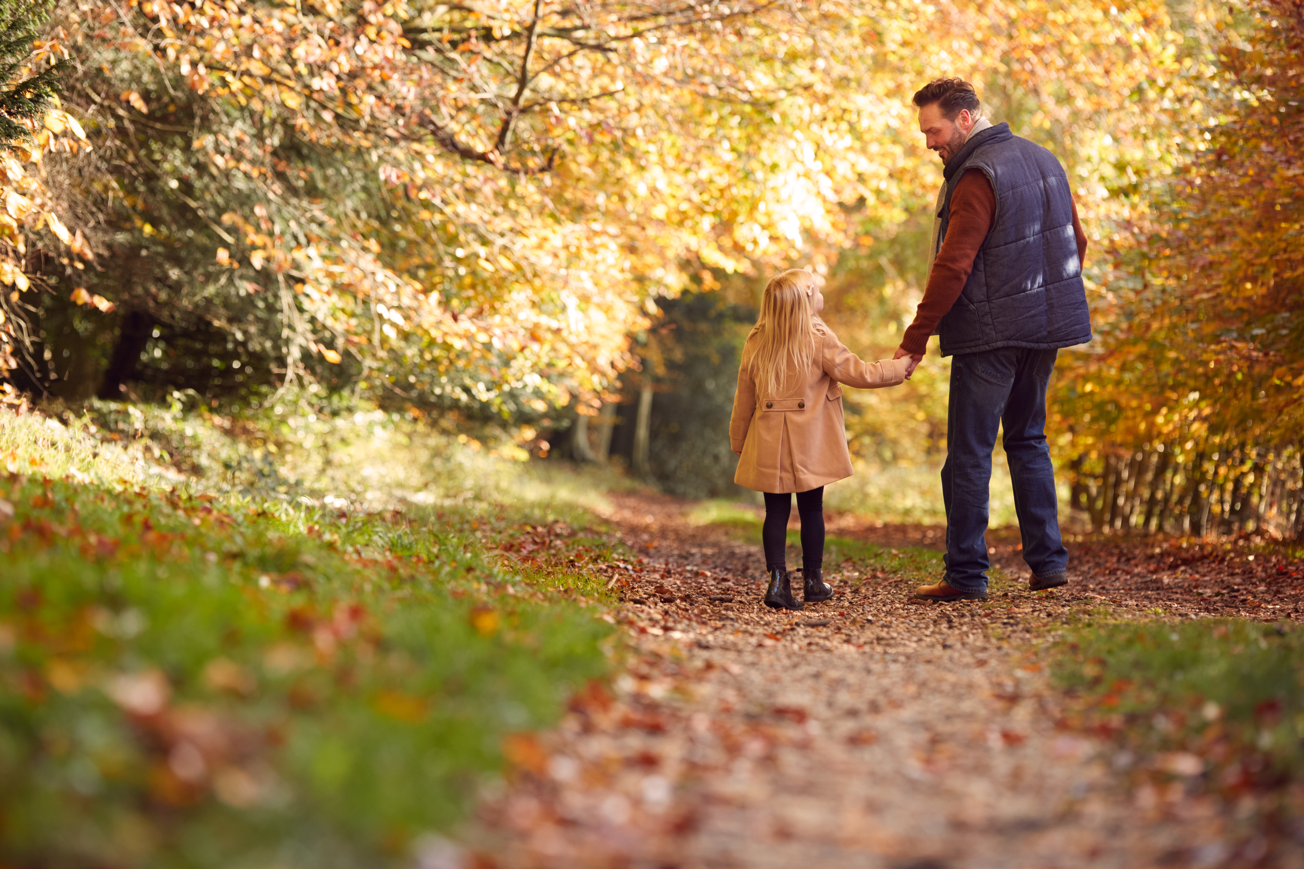 Mand holder barn i hånden i en efterårsskov
