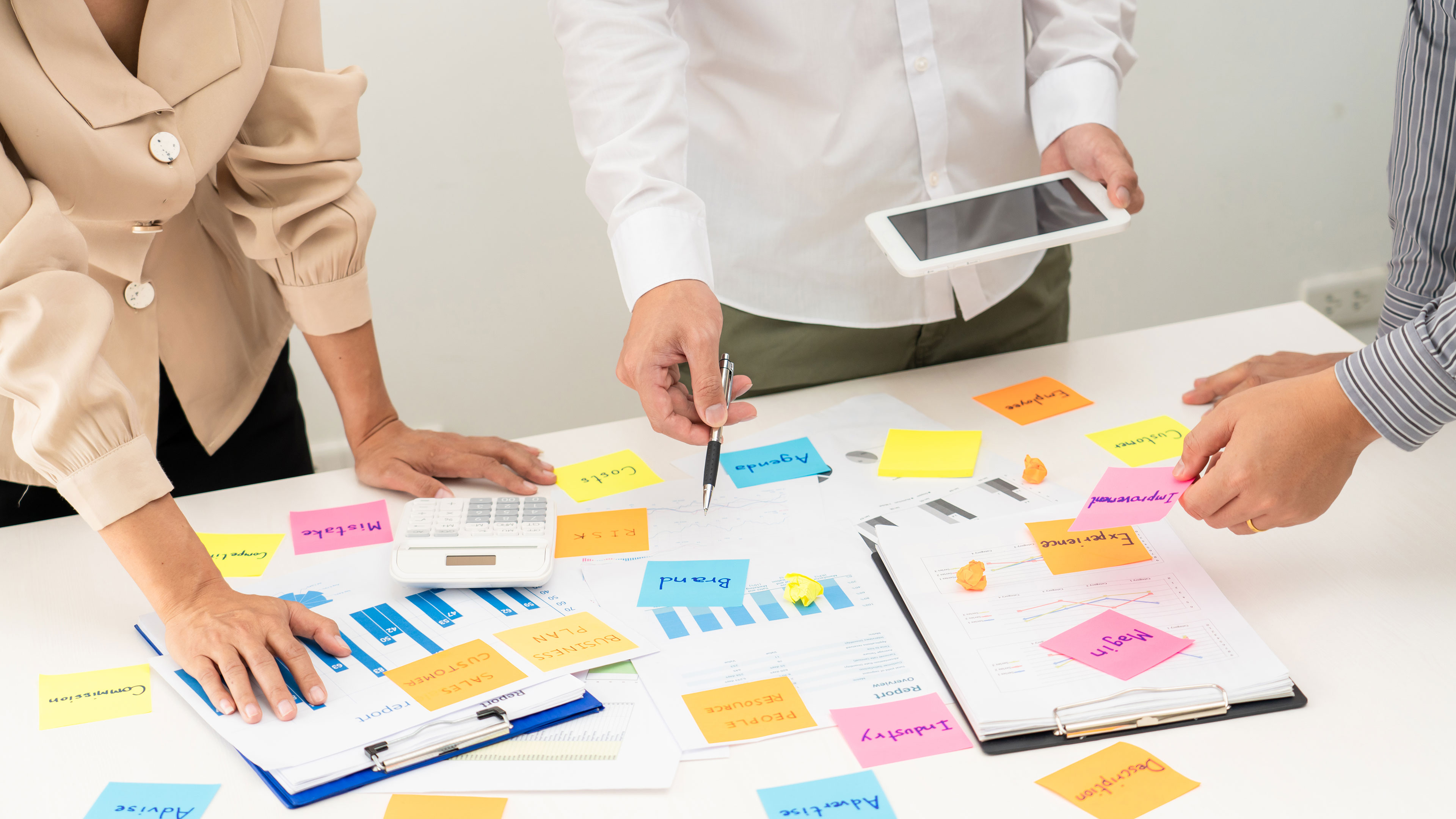 Folk stående over et skrivebord med masser af post-it sedler // Foto: Colourbox